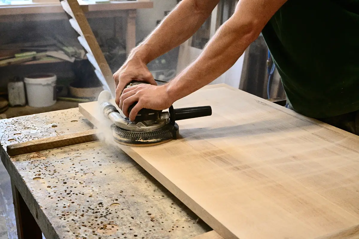 In der Schreinerei oder Tischlerei ist ein Bildausschnitt während eines Abschleiffprozesses zu sehen, bei dem auch Eichenstaub etwas aufgewirbelt wird.